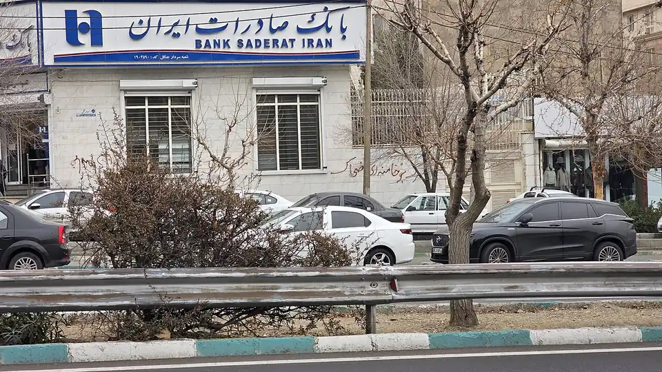 A Bank Saderat Iran branch with protest graffiti on its wall, parked cars in front