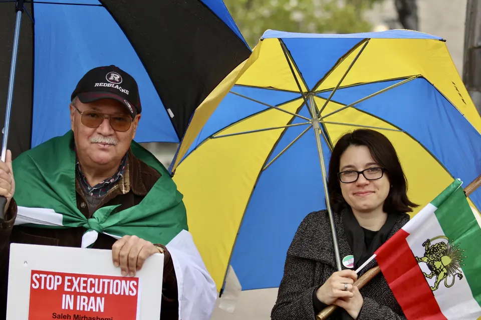 Two demonstrators holding an Iranian lion and sun flag and a placard reading Stop executions in Iran