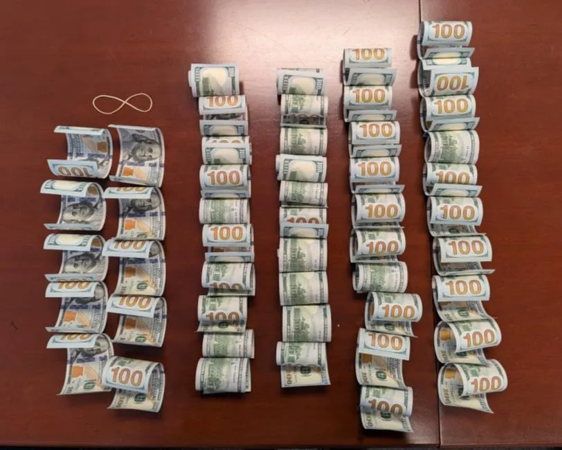 Rows of rolled one-hundred-dollar bills laid out on a wooden table
